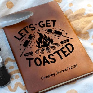 Può includere: Diario di campeggio in pelle marrone con le parole "LET'S GET TOASTED" e una grafica di falò. Il diario include il testo "Camping Journal 2026" e le date "24/07" e "365". Una piuma è appoggiata sul diario.