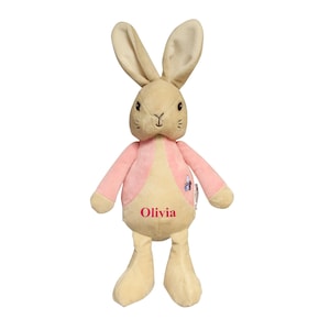 May include: A plush beige rabbit toy with pink fabric on its torso. The rabbit has a pink nose and black eyes. The toy is embroidered with the name "Olivia".