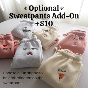 May include: Six pairs of sweatpants with different embroidered designs: a smiley face, stars, a heart, a rainbow, a flower, and a pizza slice. The text "Optional Sweatpants Add-On +$10" is at the top of the image. The text "Choose a fun shape to be embroidered on the sweatpants." is at the bottom of the image.
