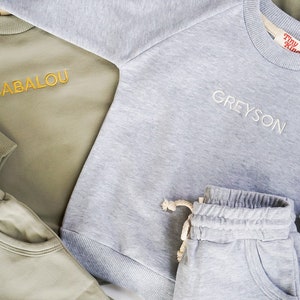Pode incluir: Dois conjuntos de roupa para crian&ccedil;as combinando. Um conjunto &eacute; cinza com o nome Greyson bordado na camisa de frio. O outro conjunto &eacute; verde com o nome Babalou bordado na camisa de frio. Ambos os conjuntos incluem uma camisa de frio e cal&ccedil;as de moletom.