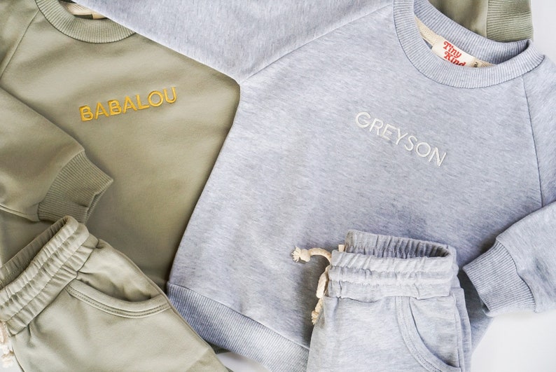 Pode incluir: Dois conjuntos de roupa para crian&ccedil;as combinando. Um conjunto &eacute; cinza com o nome Greyson bordado na camisa de frio. O outro conjunto &eacute; verde com o nome Babalou bordado na camisa de frio. Ambos os conjuntos incluem uma camisa de frio e cal&ccedil;as de moletom.