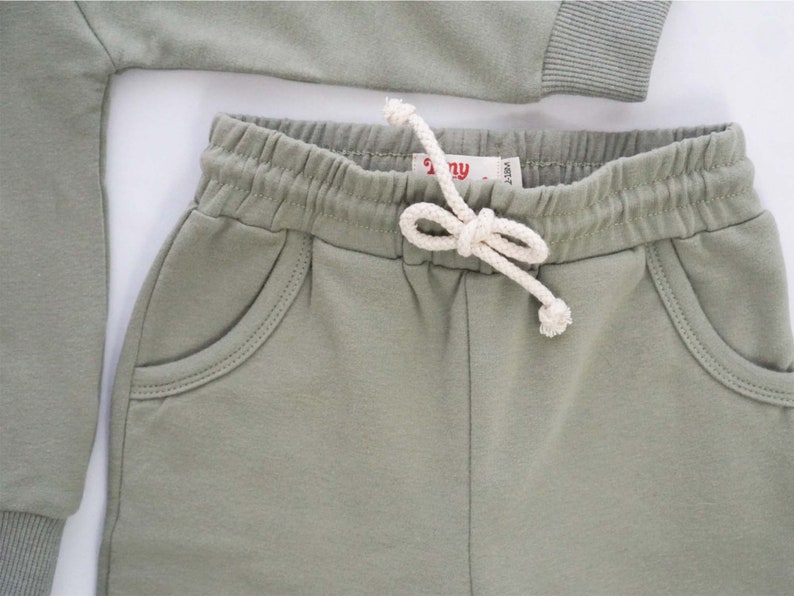 Pode incluir: Um par de cal&ccedil;as de moletom verde com cord&atilde;o branco e dois bolsos frontais. As cal&ccedil;as de moletom t&ecirc;m uma cintura canelada.
