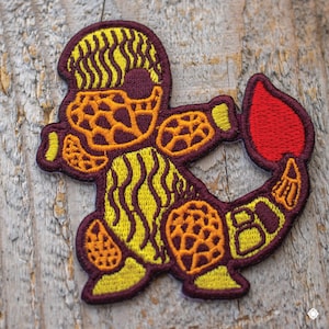 May include: A yellow and brown embroidered patch of a cartoon creature with a red heart in its hand. The creature has a striped body and a textured head.