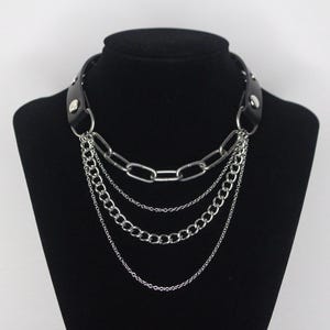 May include: A black leather choker necklace with multiple silver chains. The chains are of different lengths and thicknesses, creating a layered look.