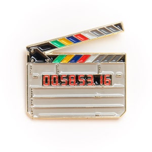 Peut inclure: Clap de cinéma en métal doré avec une poignée noire et des rayures colorées. Le clap de cinéma a un affichage numérique de minuterie affichant "00:58:53.16".