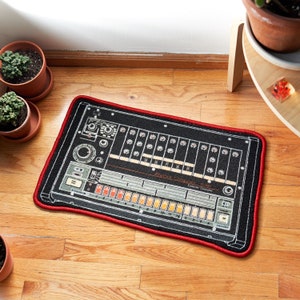 Könnte beinhalten: Schwarzer und roter Teppich mit einer Grafik einer Vintage-Drum-Machine. Die Drum-Machine hat ein schwarz-weißes Design mit dem Text "Rhythm Composer Drum" und "Control Console".