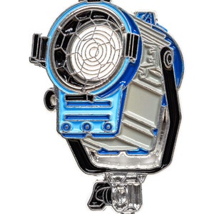 May include: A silver metal pin of a blue and silver movie studio spotlight with a black handle and a black and silver grid.