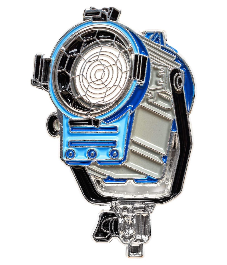 May include: A silver metal pin of a blue and silver movie studio spotlight with a black handle and a black and silver grid.