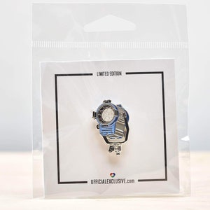 May include: A silver and blue enamel pin featuring a movie spotlight. The pin is packaged in a clear plastic bag with a white card that reads "Limited Edition" and "officialexclusive.com".