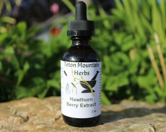 Könnte beinhalten: Eine 60 ml Flasche Teton Mountain Herbs Hawthorn Berry Extract. Die Flasche ist aus braunem Glas mit einem schwarzen Tropferdeckel und einem weißen Etikett mit schwarzem Text. Das Etikett zeigt eine Zeichnung eines Mörser und Stößers mit einem Zweig von Weißdornbeeren.