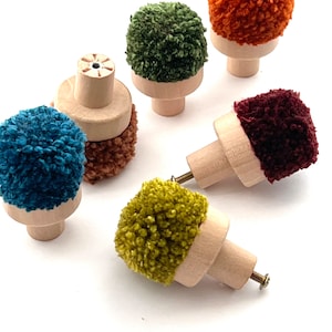 May include: Six wooden knobs with colorful pom-poms. The knobs are made of natural wood and have a simple, minimalist design. The pom-poms are made of yarn and come in a variety of colors, including green, orange, blue, burgundy, and yellow.