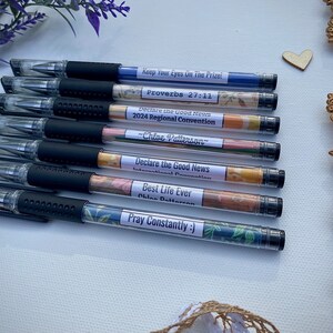 Peut inclure: Huit stylos noirs et transparents avec des &eacute;tiquettes &agrave; motifs floraux color&eacute;s. Les &eacute;tiquettes comportent du texte qui comprend "Keep Your Eyes On The Prize", "Proverbes 27:11", "Declare the Good News", "Convention R&eacute;gionale 2024", "-Chloe Patterson", "Convention Internationale", "Best Life Ever", "Chloe Patterson", et "Priez Constamment :)".