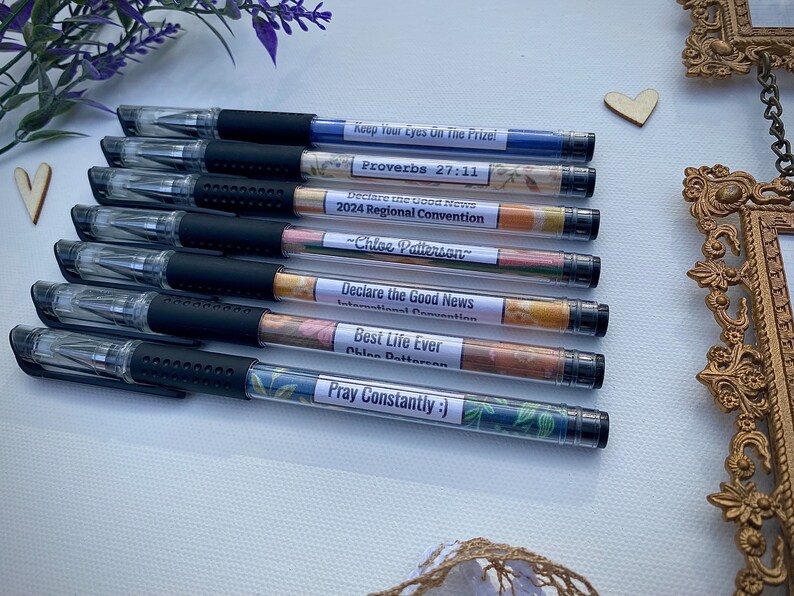 Peut inclure: Huit stylos noirs et transparents avec des &eacute;tiquettes &agrave; motifs floraux color&eacute;s. Les &eacute;tiquettes comportent du texte qui comprend "Keep Your Eyes On The Prize", "Proverbes 27:11", "Declare the Good News", "Convention R&eacute;gionale 2024", "-Chloe Patterson", "Convention Internationale", "Best Life Ever", "Chloe Patterson", et "Priez Constamment :)".