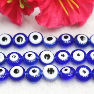 Puede incluir: Una hebra de cuentas de vidrio azul con dise&ntilde;os de ojo turco blanco y negro. Las cuentas son redondas y tienen un acabado brillante.