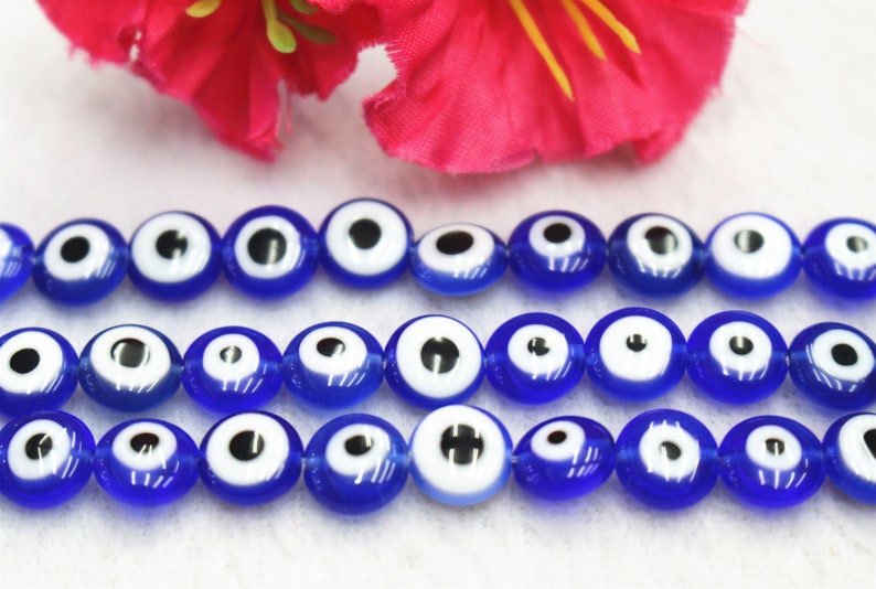Puede incluir: Una hebra de cuentas de vidrio azul con dise&ntilde;os de ojo turco blanco y negro. Las cuentas son redondas y tienen un acabado brillante.
