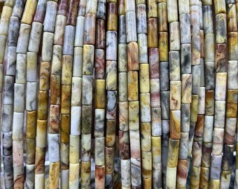 May include: Close-up of a collection of cylindrical beads in various colors, including beige, brown, gray, and yellow. The beads are strung together, creating a textured surface. The beads appear to be made of stone.