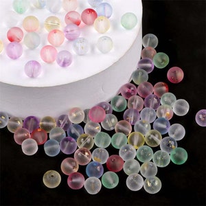 May include: Assortment of small, round, translucent glass beads with gold flecks. The beads are in various pastel colors, including pink, blue, green, and purple.