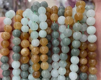 Puede incluir: Cadenas de cuentas de piedras preciosas en varios colores, incluyendo blanco, gris y ámbar. Las cuentas redondas están ensartadas en hilo verde. Las cuentas pulidas tienen un aspecto natural y terroso. Las cuentas son lisas.