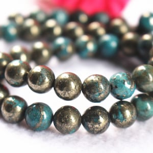 May include: A strand of round, teal blue and gold beads. The beads are made of pyrite and have a speckled, metallic finish.