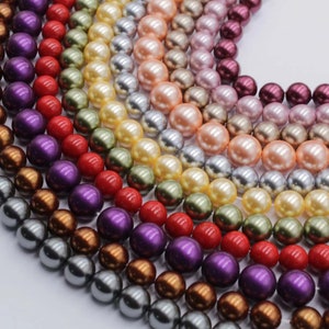 Op de afbeelding: Een verzameling parel kralen in verschillende kleuren, waaronder rood, paars, bruin, grijs en crème. De kralen zijn in een halve cirkel gerangschikt, met de grootste kralen onderaan en de kleinste kralen bovenaan.
