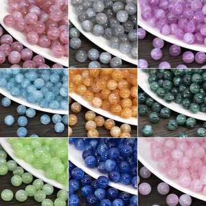 May include: A collection of nine square panels displaying round, translucent beads in various colors including pink, gray, purple, light blue, orange, dark green, light green, dark blue, and soft pink, each featuring a subtle internal shimmer.