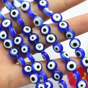Puede incluir: Una hebra de cuentas de vidrio azul con dise&ntilde;os de ojo turco blanco y negro. Las cuentas son redondas y tienen un acabado brillante.