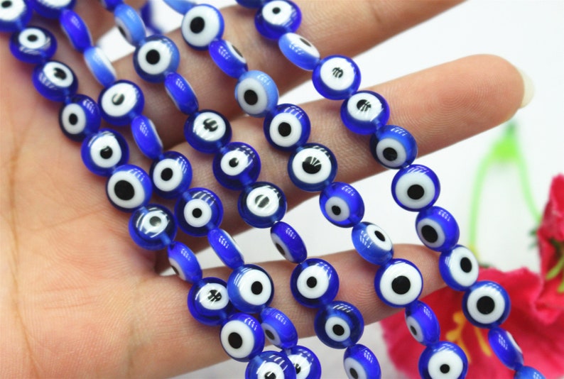 Puede incluir: Una hebra de cuentas de vidrio azul con dise&ntilde;os de ojo turco blanco y negro. Las cuentas son redondas y tienen un acabado brillante.
