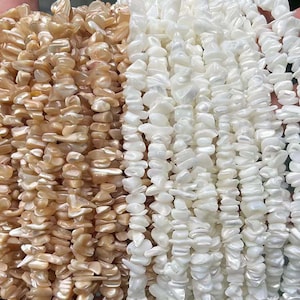 Puede incluir: Dos hebras de cuentas de concha plana, de forma irregular e iridiscente. Una hebra es de color marrón claro y la otra es blanca.