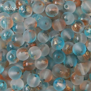 May include: A close-up of a collection of small, round, frosted glass beads. The beads are a mix of light blue and clear with gold flecks. The beads are scattered randomly.