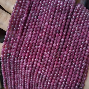 May include: A strand of pink ruby beads, faceted and round, with a smooth, polished finish. The beads are strung on a clear thread and are ready for jewellery making.