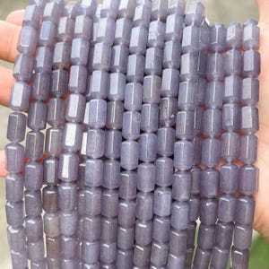 May include: A collection of light purple, cylindrical beads arranged in multiple vertical strands. Each bead features a smooth, polished surface with a consistent rectangular shape and rounded edges, creating a uniform appearance across the entire set.