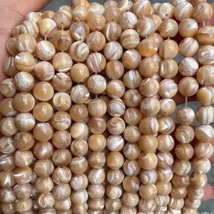May include: A strand of round, white and brown shell beads. The beads have a natural, iridescent sheen.