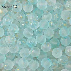 May include: A close-up of a group of light blue glass beads with gold flecks. The beads are round and have a frosted finish.