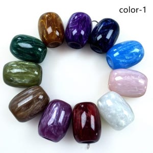 Puede incluir: Una colección de once cuentas en forma de barril dispuestas en círculo, cada una con un acabado brillante y jaspeado en colores distintos que incluyen oro, morado, azul oscuro, azul brillante, rosa claro, blanco, rojo, violeta, marrón, verde oliva y verde oscuro. El texto dice color-1.