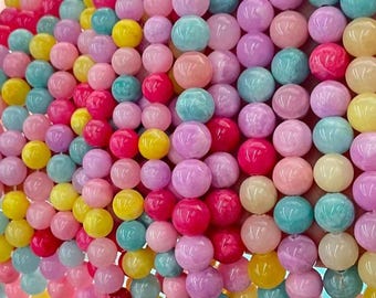 May include: A close-up of a collection of colorful round beads in various shades of pink, purple, yellow, blue, and peach. The beads are strung together, creating a textured and vibrant display, suitable for jewelry making or crafts.