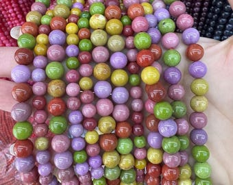 Puede incluir: Hileras de cuentas de piedras preciosas de colores en varios tamaños y tonos, incluyendo rojo, verde, amarillo, morado y rosa. Las cuentas son redondas y parecen estar ensartadas, probablemente para hacer joyas o manualidades. Vista de cerca.