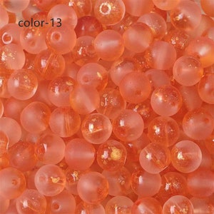 May include: A close-up of a group of small, round, translucent orange beads with gold flecks. The beads are scattered on a surface.