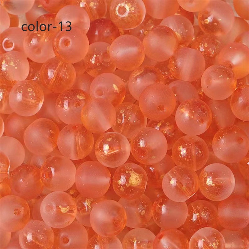May include: A close-up of a group of small, round, translucent orange beads with gold flecks. The beads are scattered on a surface.
