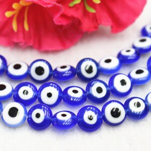 Puede incluir: Una hebra de cuentas de vidrio azul con dise&ntilde;os de ojo turco blanco y negro. Las cuentas est&aacute;n enhebradas en un hilo transparente.