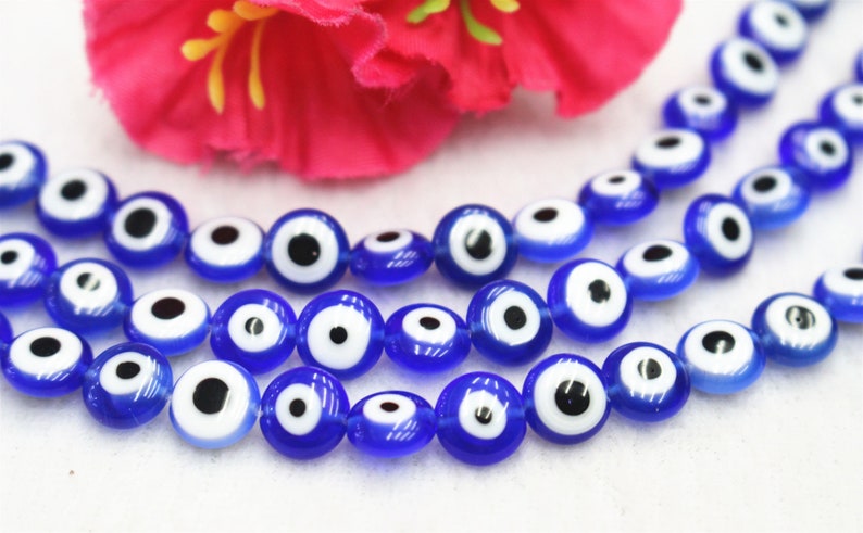 Puede incluir: Una hebra de cuentas de vidrio azul con dise&ntilde;os de ojo turco blanco y negro. Las cuentas est&aacute;n enhebradas en un hilo transparente.