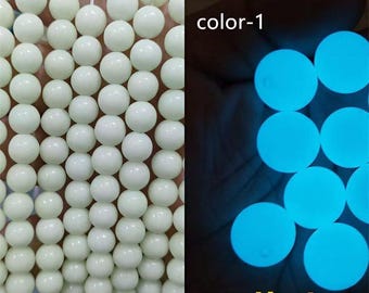 Op de afbeelding: Een streng witte glow-in-the-dark kralen. De kralen zijn rond en glad. De afbeelding toont ook een close-up van de kralen die blauw gloeien in het donker. De tekst "color-1" is zichtbaar in de afbeelding.