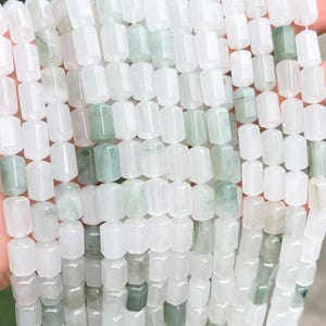 May include: A collection of cylindrical beads arranged in vertical strands. The beads are primarily translucent white with scattered inclusions of pale green and soft mint hues, featuring a smooth, polished finish and a uniform, elongated shape.