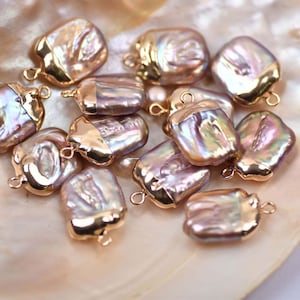 May include: A collection of 12 iridescent baroque pearl charms with gold-tone accents. The pearls are a mix of pink, purple, and white.
