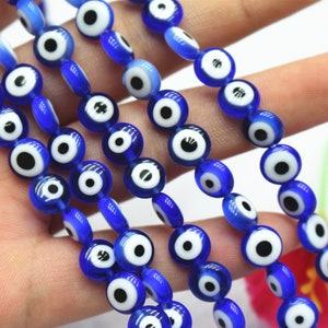 Puede incluir: Una hebra de cuentas de vidrio azul con dise&ntilde;os de ojo turco blanco y negro. Las cuentas son redondas y tienen un acabado brillante.