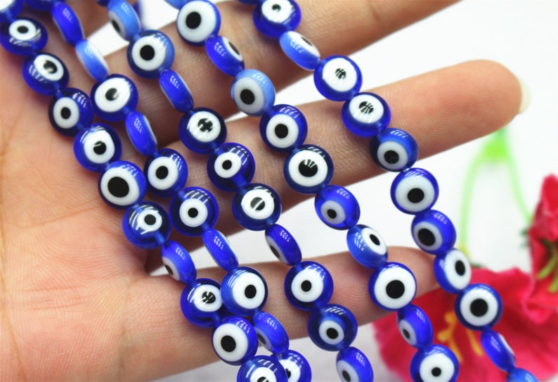Puede incluir: Una hebra de cuentas de vidrio azul con dise&ntilde;os de ojo turco blanco y negro. Las cuentas son redondas y tienen un acabado brillante.