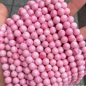 Peut inclure: Un brin de perles de pierres précieuses roses et blanches. Les perles sont rondes et ont une finition lisse et polie.