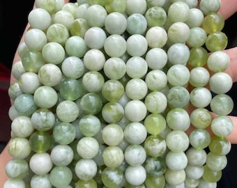 May include: A strand of light green jade beads. The beads are round and smooth, with a slightly translucent appearance. The beads are strung on a clear elastic cord.