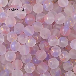 May include: A close-up of a pile of translucent, pastel purple and pink beads with gold flecks. The beads are round and have a frosted finish.