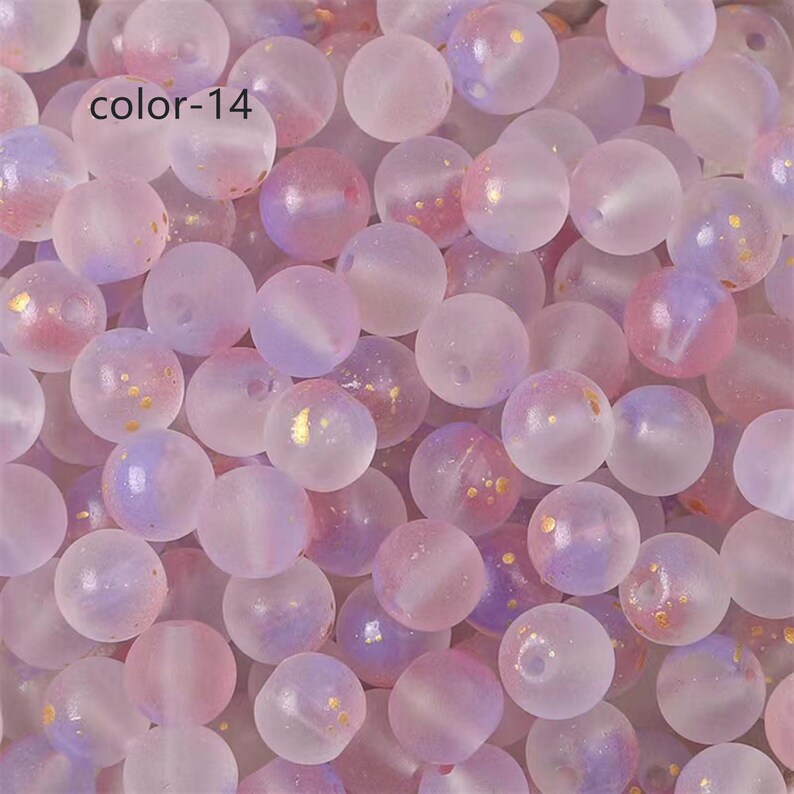 May include: A close-up of a pile of translucent, pastel purple and pink beads with gold flecks. The beads are round and have a frosted finish.