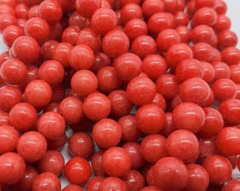 May include: A close-up of a pile of smooth, round, red coral beads. The beads are all the same size and have a slightly glossy finish.